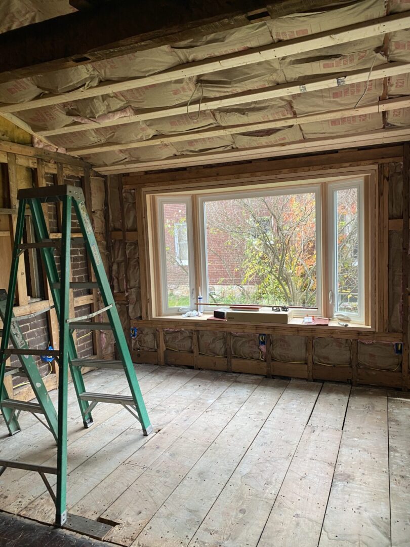 A ladder in the middle of a room with windows.